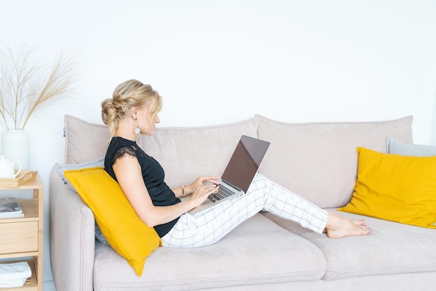 Mulher sorridente sentada no sofá assistindo webinar no laptop jovem feliz em uso