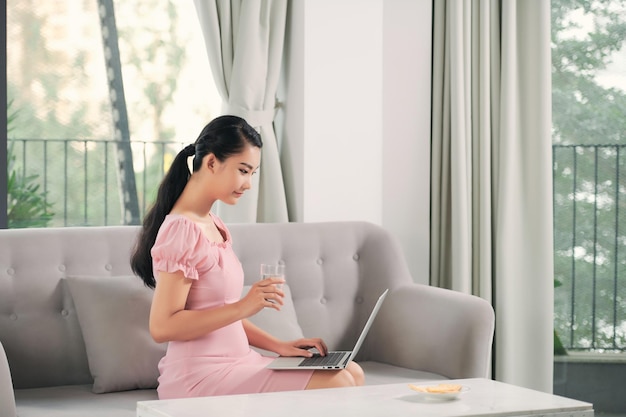 Mulher sorridente sentada no sofá relaxando enquanto navega no site de compras online