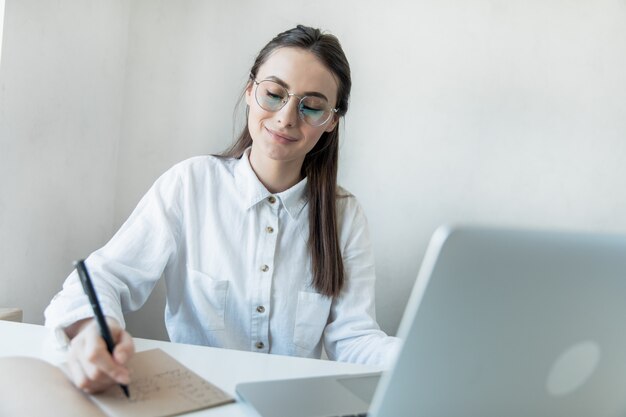 Mulher sorridente, sentado em sua mesa no escritório. Mulher de negócios feliz sentado no escritório com os dedos tocando seu queixo.