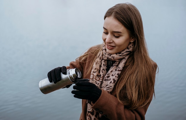 Foto mulher sorridente servindo uma bebida quente à beira do lago