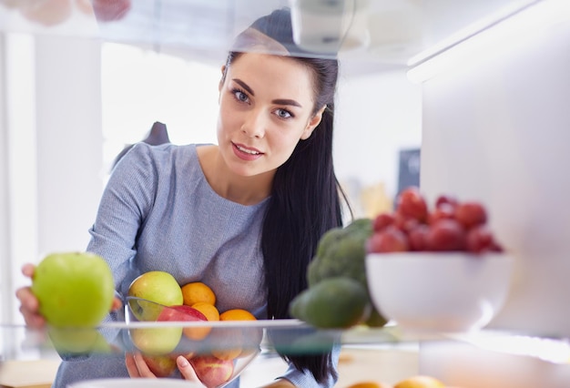 Mulher sorridente, tirando uma fruta fresca da geladeira, o conceito de comida saudável.