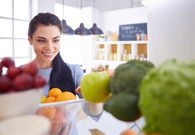 Mulher sorridente tirando uma fruta fresca do conceito de comida saudável da geladeira