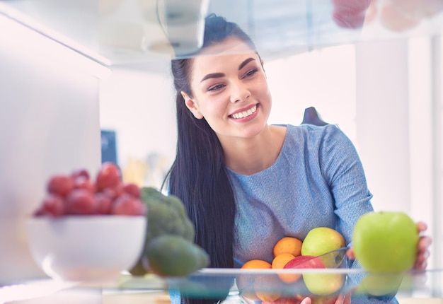 Mulher sorridente tirando uma fruta fresca do conceito de comida saudável da geladeira