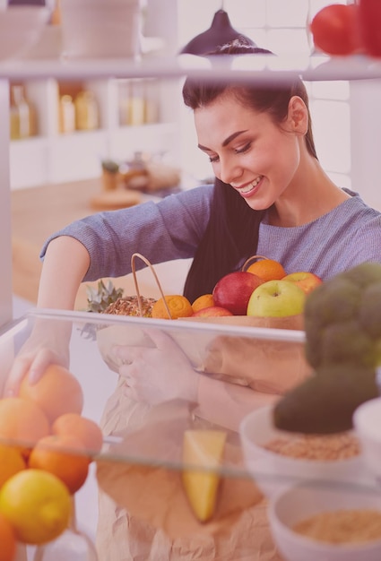 Mulher sorridente tirando uma fruta fresca do conceito de comida saudável da geladeira