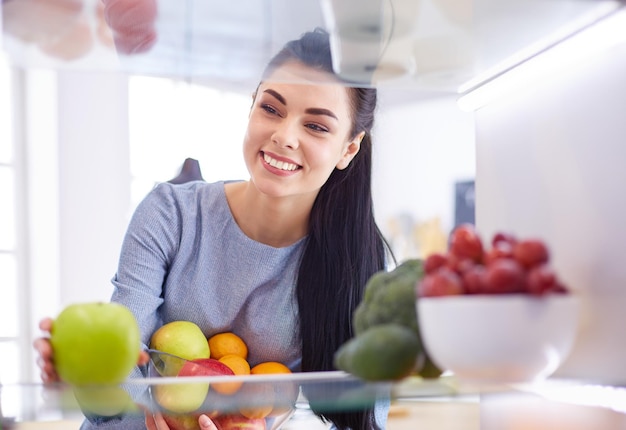 Mulher sorridente tirando uma fruta fresca do conceito de comida saudável da geladeira