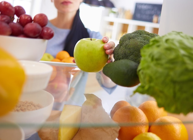 Mulher sorridente tirando uma fruta fresca do conceito de comida saudável da geladeira