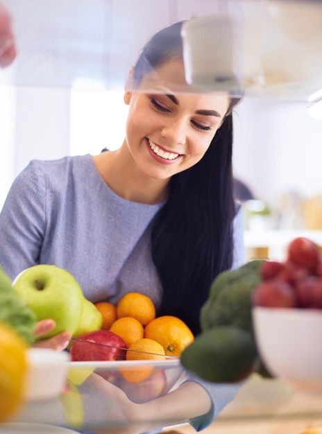 Mulher sorridente tirando uma fruta fresca do conceito de comida saudável da geladeira