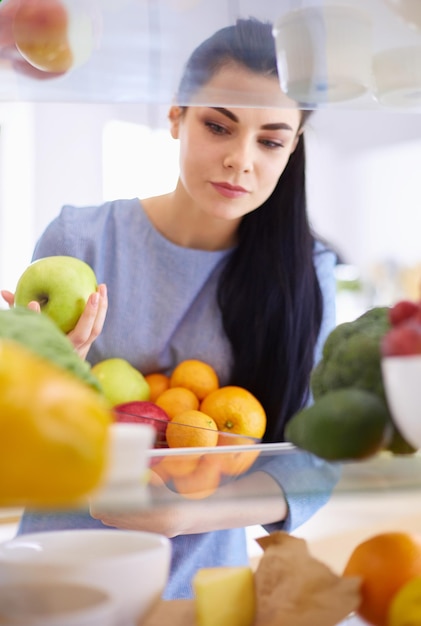 Mulher sorridente tirando uma fruta fresca do conceito de comida saudável da geladeira