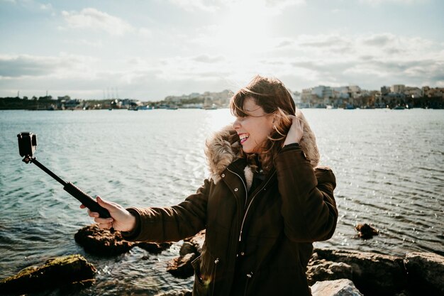Foto mulher sorridente tirando uma selfie com a câmera enquanto está de pé contra o lago