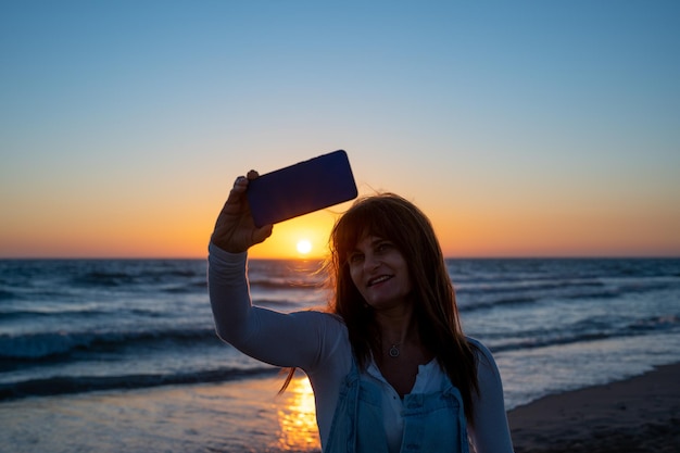 Mulher sorridente tomando uma selfie com um pôr do sol na praia