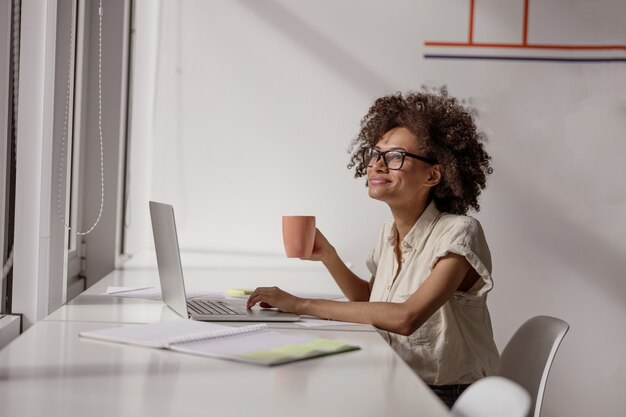 Foto mulher sorridente, trabalhando com o laptop e segurando o café na mão