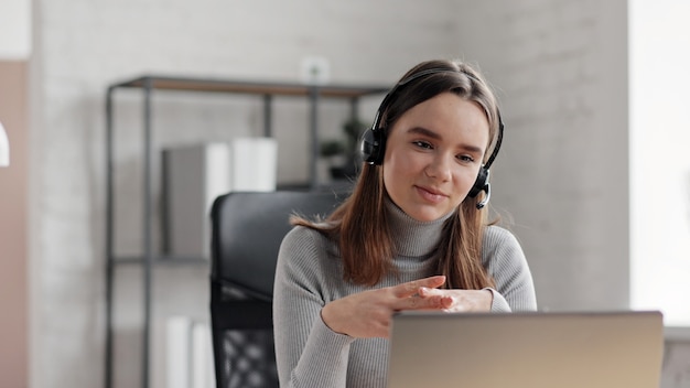 Foto mulher sorridente usando laptop e fone de ouvido sem fio para reunião online, chamada de vídeo, videoconferência.