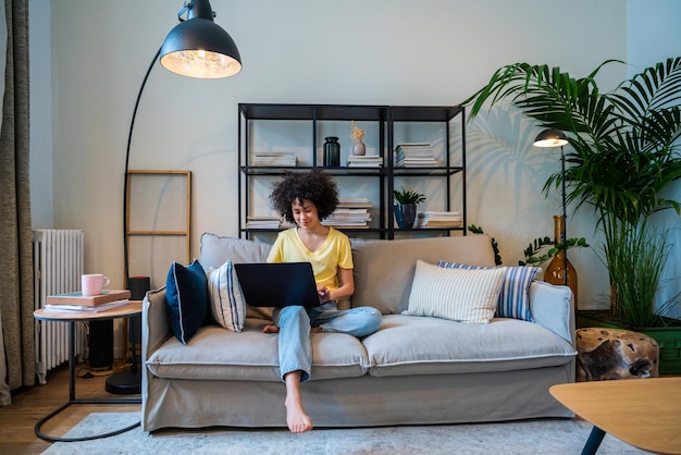 Mulher sorridente usando laptop enquanto está sentada no sofá em casa