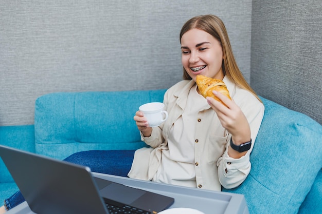 Mulher sorridente usando laptop para verificar notícias de e-mail on-line enquanto está sentado no sofá trabalhando no computador escrevendo blog ou assistindo webinar estudando em casa