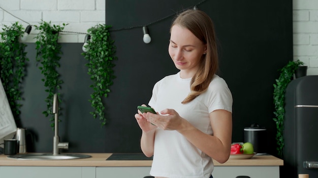 Mulher sorridente usando smartphone na cozinha