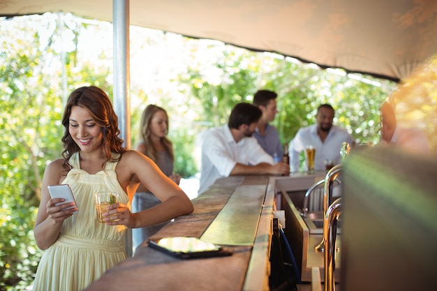 Mulher sorridente usando telefone celular enquanto toma um copo de cerveja