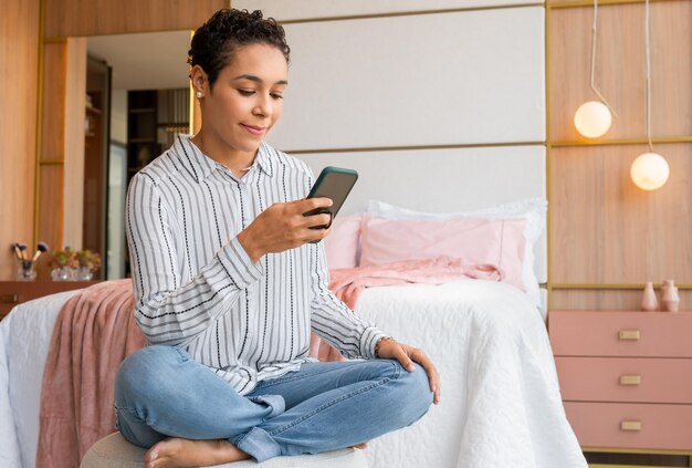 Foto mulher sorridente usando telefone celular sentada na cama