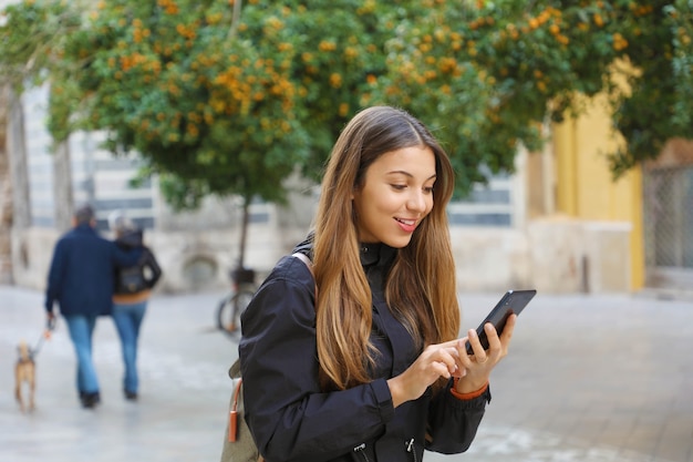 Mulher sorridente usando um telefone celular em uma rua com tangerinas na cidade