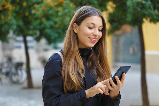 Mulher sorridente usando um telefone celular em uma rua da cidade