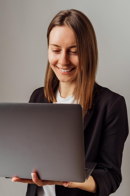 Mulher sorridente vestindo jaqueta preta está trabalhando no laptop enquanto sorri