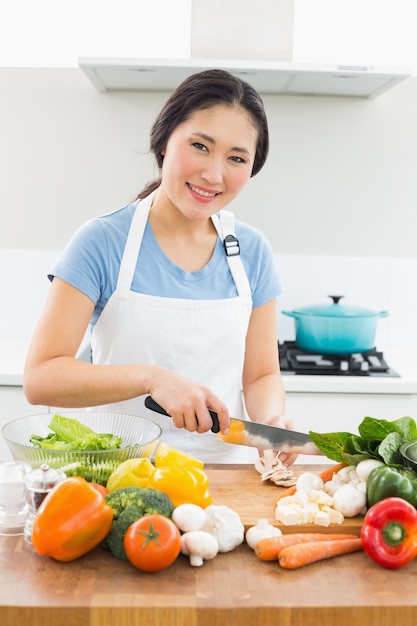 Mulher sorrindo cortando vegetais na cozinha