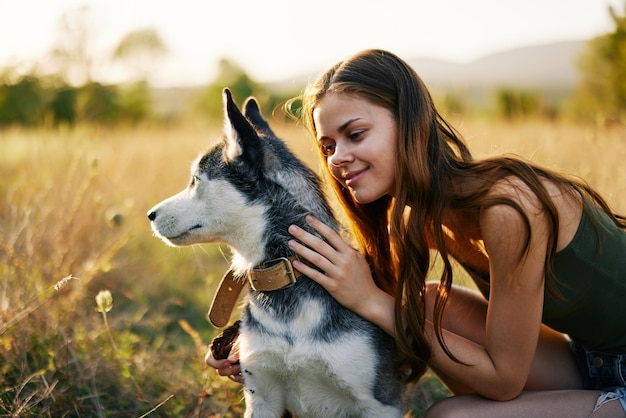 Mulher sorrindo e abraçando seu cachorro sentado em um campo com um cachorro bassê sorrindo enquanto passa o tempo ao ar livre com um cachorro amigo no outono ao pôr do sol enquanto viaja