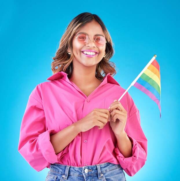 Foto mulher sorrindo e bandeira de orgulho em retrato de estúdio com óculos de sol de moda e sinal para direitos humanos por fundo azul gen z garota estudante lésbica e feliz em protesto apoio e liberdade para lgbtq