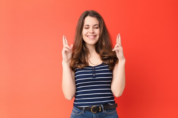 Mulher sorrindo e cruzando ansiosamente os dois dedos, sentindo-se preocupada e desejando ou esperando boa sorte