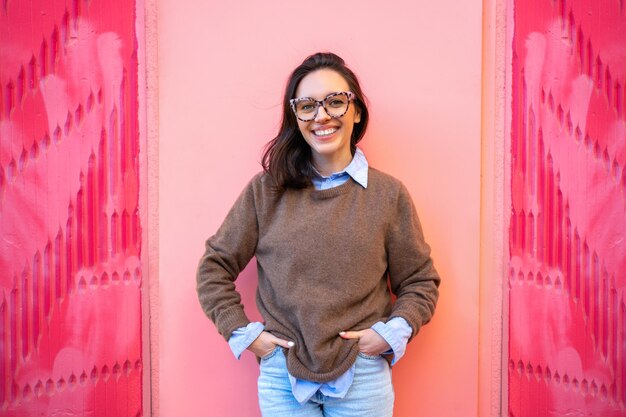 Mulher sorrindo e posando para foto perto da parede rosa na rua