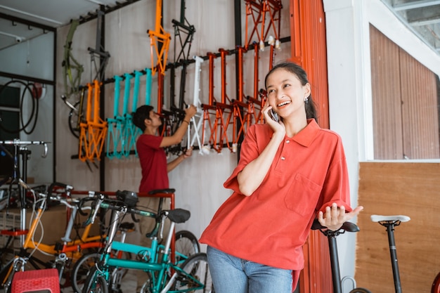 Mulher sorrindo feliz enquanto conversa usando um telefone celular em uma loja de bicicletas