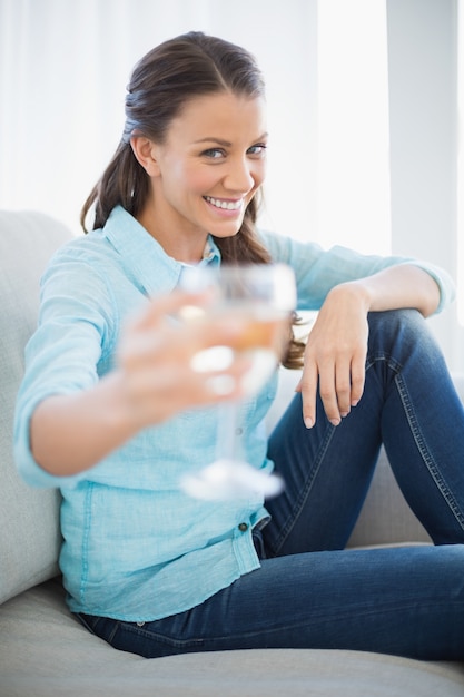 Mulher sorrindo mostrando copo de vinho branco na câmera