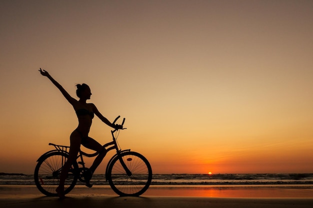 Mulher sozinha e saudável anda de bicicleta na praia vazia do pôr do sol de goa índia