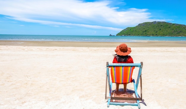 Mulher sozinha relaxando em uma cadeira de madeira em uma praia tropical apreciando o mar e o céu