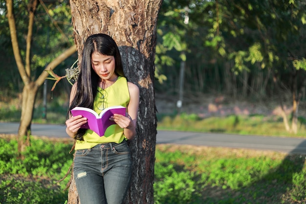 mulher stading na árvore e lendo um livro no parque