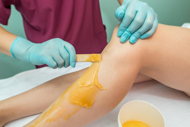 Mulher submetida a procedimento de depilação da perna com pasta de açúcar no salão Cuidados com a pele remover cabelo com pasta de açúcar
