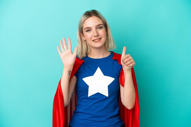 Mulher super-heroína caucasiana isolada em fundo azul contando seis com os dedos