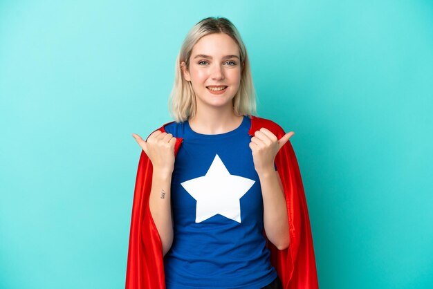 Mulher super-heroína caucasiana isolada em um fundo azul com gesto de polegar para cima e sorrindo