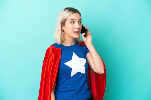Mulher super-heroína, caucasiana, isolada em um fundo azul, conversando com o celular