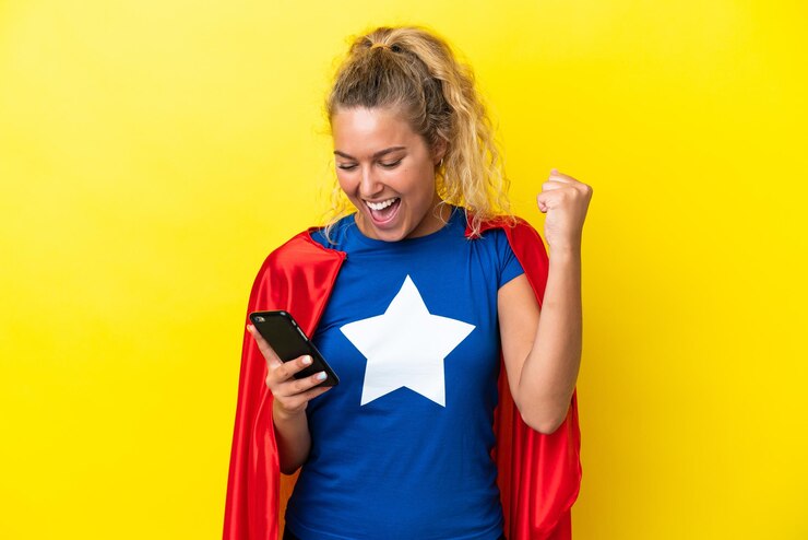 Foto mulher super-heroína isolada em fundo amarelo usando telefone celular e fazendo gesto de vitória