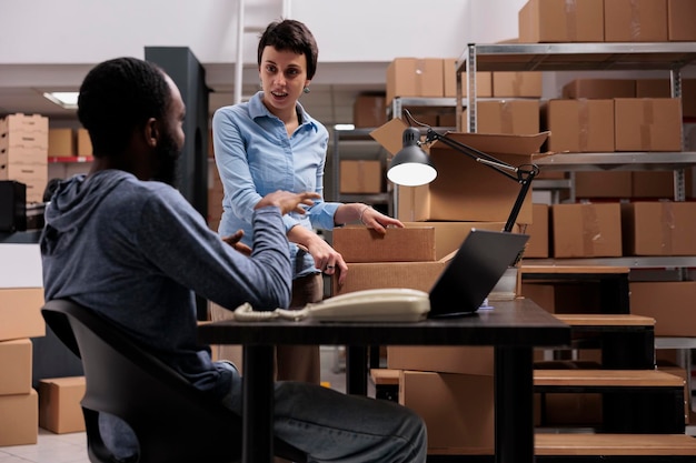 Mulher supervisora colocando o pedido do cliente em caixa de papelão preparando pacotes para entrega enquanto discute a logística de remessa com o gerente afro-americano, trabalhando no armazém. centro de distribuição