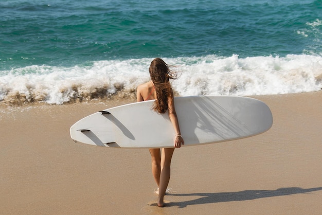 Mulher surfista andando com prancha de surf na praia tropical