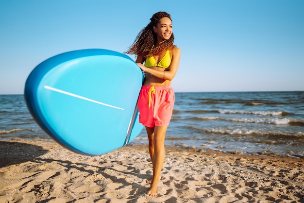 Mulher surfista caminha com uma prancha na praia de areia Esporte radical Viagens estilo de vida de fim de semana