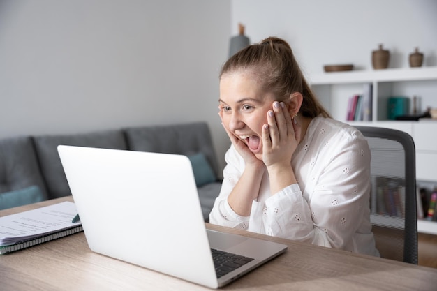 Mulher surpreendida assistindo bons resultados no laptop com as mãos no rosto