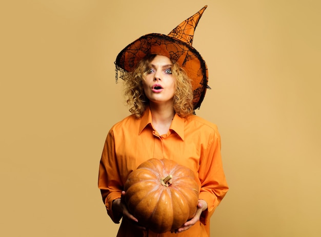 Mulher surpreendida com chapéu de bruxa com abóbora. Garota com fantasia de halloween com jack-o-lantern. Férias de Halloween.
