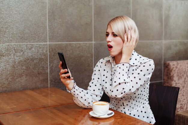 Mulher surpreendida no café olhando para smartphone