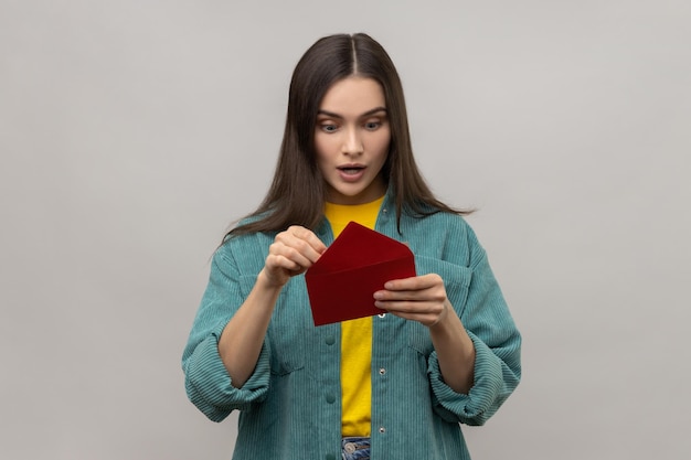 Mulher surpresa espantada segurando o envelope romântico vermelho e olhando para a carta com a boca aberta