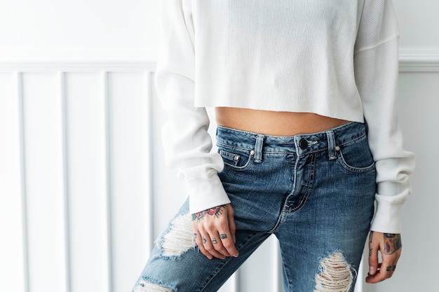 Mulher tatuada em um top crop branco e jeans rasgados