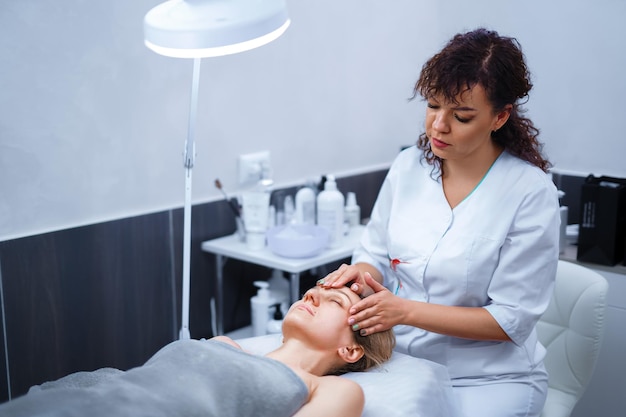 Mulher tendo uma massagem facial gua sha com massageador de pedra de jade natural no salão