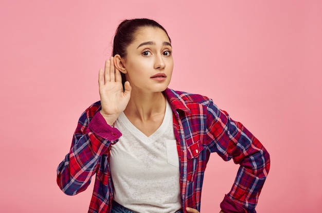 Mulher tenta ouvir, parede rosa, emoção. expressão facial, pessoa do sexo feminino olhando para a câmera no estúdio, conceito emocional, sentimentos