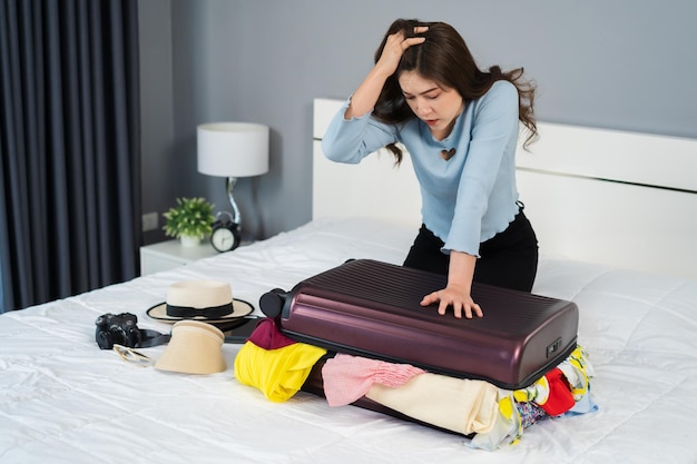 Foto mulher tentando fechar a mala cheia na cama